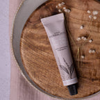 Enriching Hand Cream tube lying on a wooden board with dried flowers