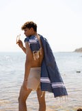 Man standing by the sea with Navy and White Ipanema Fouta towel draped over his shoulder