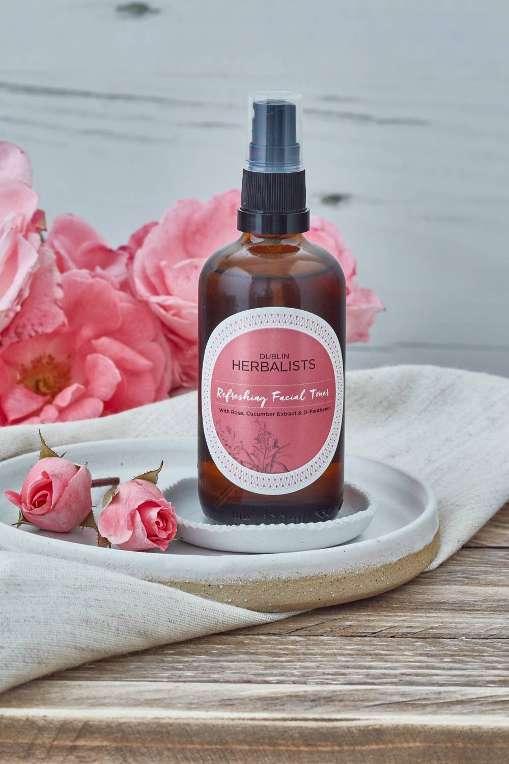 Dublin Herbalists Rose and Cucumber Refreshing Facial Toner 100ml - bottle standing on a ceramic plate with pink roses