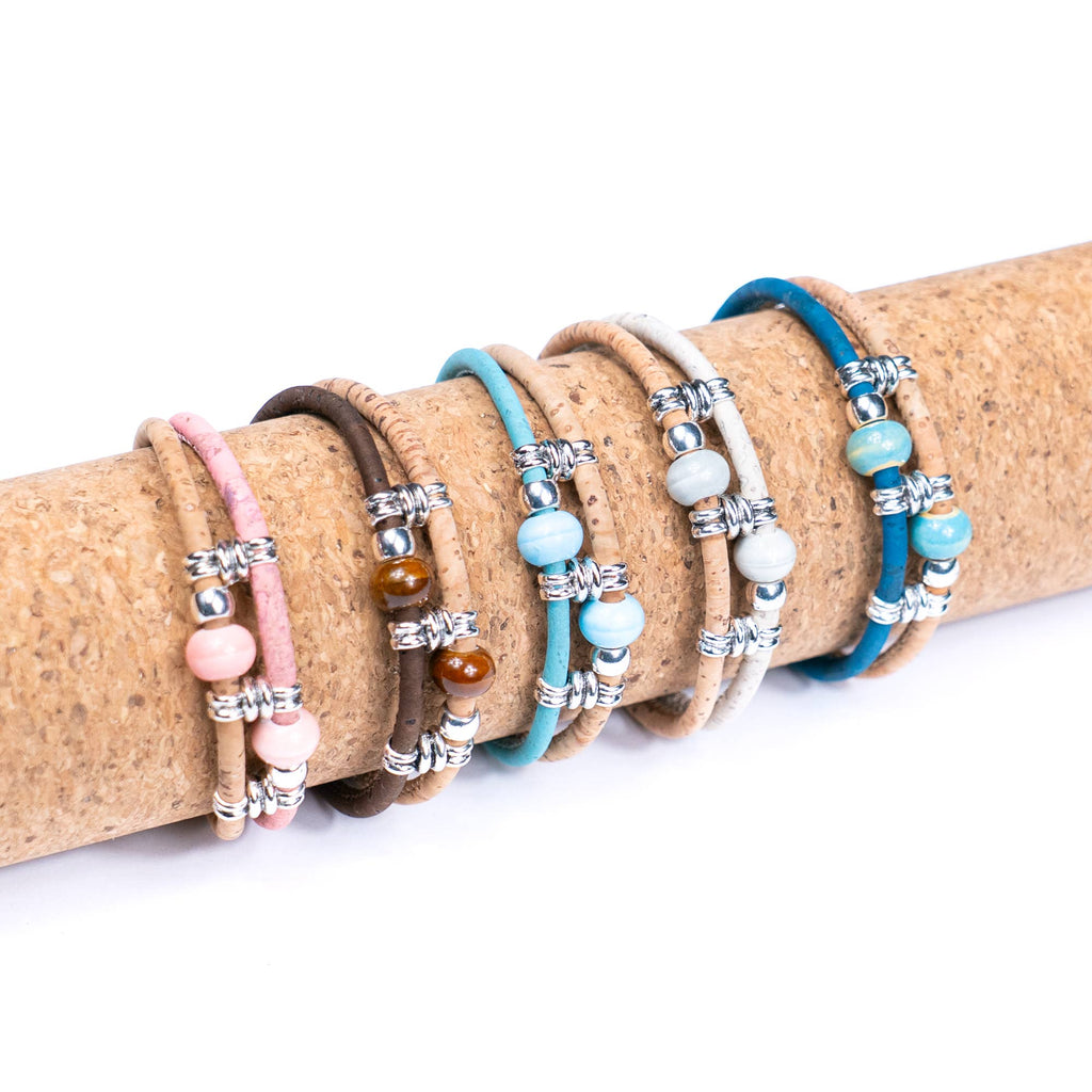 Meninas Bonitas Cork Colourful Ceramic Bead Handmade Bracelet 18x1cm – layout – five cork bracelets in dark brown, white, light blue, royal blue, and pink displayed on a cork roll.