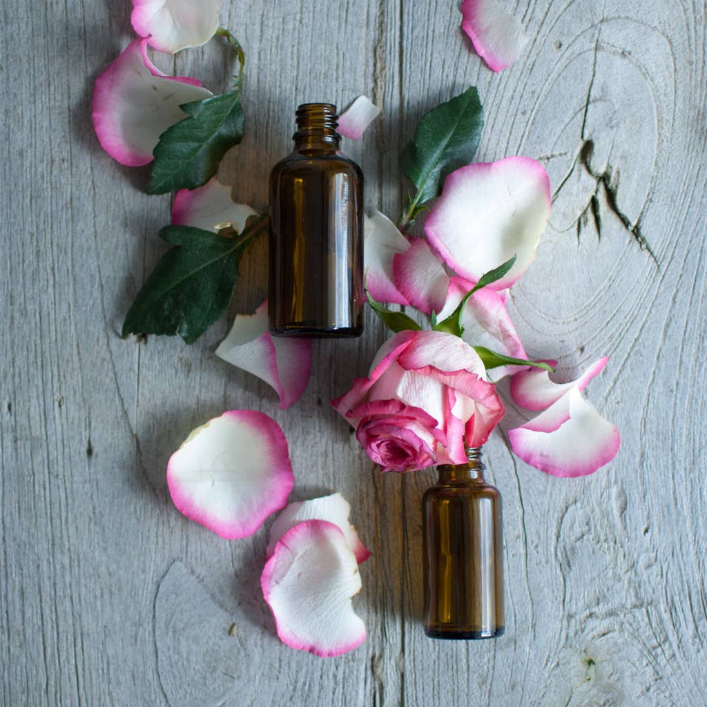 Two amber glass bottles lying on a wooden surface with scattered rose petals and leaves