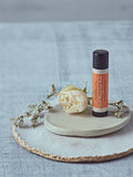 Dublin Herbalists Sweet Orange Lip Balm 5g - tube standing on a ceramic dish with a white rose